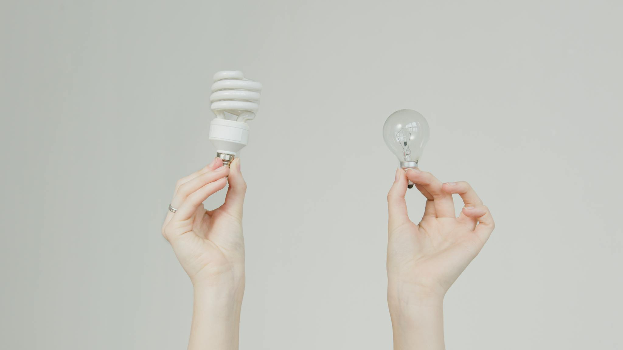 Hands hold incandescent and spiral light bulbs, symbolizing energy efficiency.